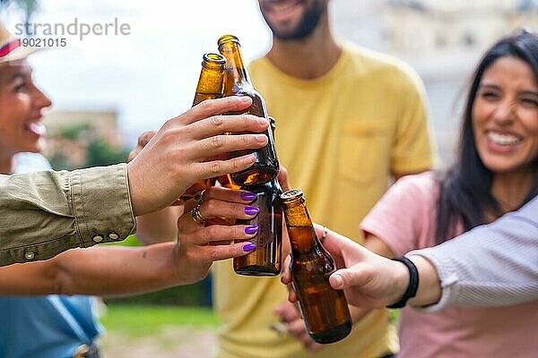 Multiethnische Gruppe von Freunden  die in einem Stadtpark mit Bier feiern und mit den Flaschen anstoßen