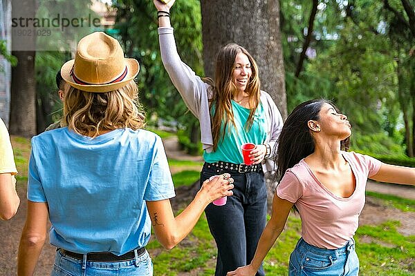 Multiethnische Gruppe von Geburtstagsparty in der Stadt Park Spaß haben und tanzen mit bunten Tassen