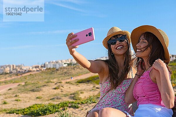 Frau Freunde mit Hut im Urlaub am Strand nehmen ein Selfie mit dem Telefon lächelnd
