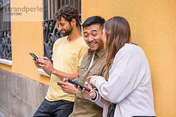 Gruppe von multirassischen Freunden  die lächelnd auf das Telefon in der Stadt schauen