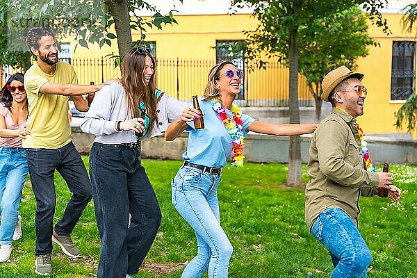 Gruppe multiethnischer Freunde auf einer Geburtstagsfeier im Stadtpark  die tanzen  Partykleidung tragen und im Sommer Sonnenbrillen tragen