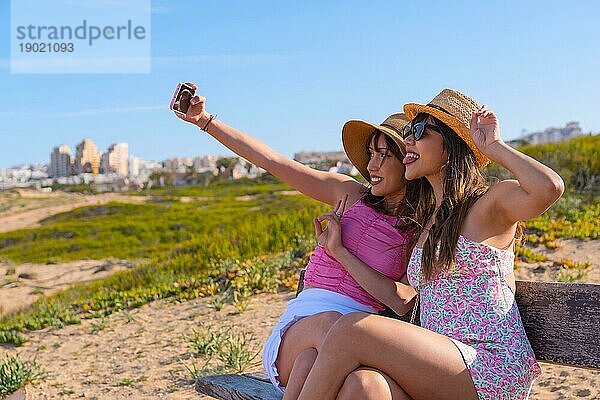 Freundinnen in Hut sehr glücklich am Strand Urlaub machen ein Selfie mit Telefon  Sommer Reise Freunde Freundschaft Konzept