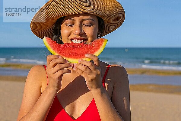 Porträt einer Frau  die am Strand eine Wassermelone isst. Nahaufnahme lächelnd mit Bikini