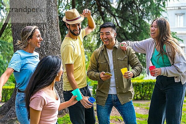 Multiethnische Gruppe von Geburtstagsfeier in der Stadt Park tanzen und lächelnd zusammen mit Bäumen und Natur