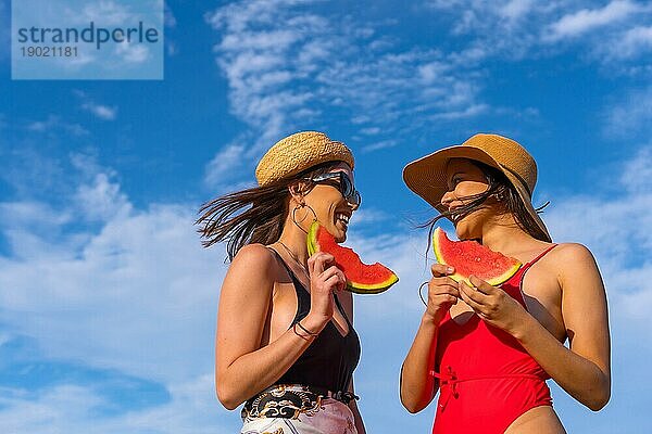 Freundinnen am Strand im Sommer beim Essen einer Wassermelone mit dem Himmel im Hintergrund  Aufnahme von unten nach oben