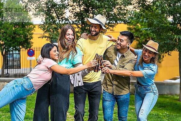 Eine multiethnische Gruppe von Freunden feiert in einem Stadtpark und stößt mit Bierflaschen an