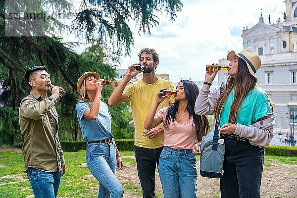 Eine multiethnische Gruppe von Freunden feiert in einem Stadtpark mit Bier. Freunde trinken kaltes Bier