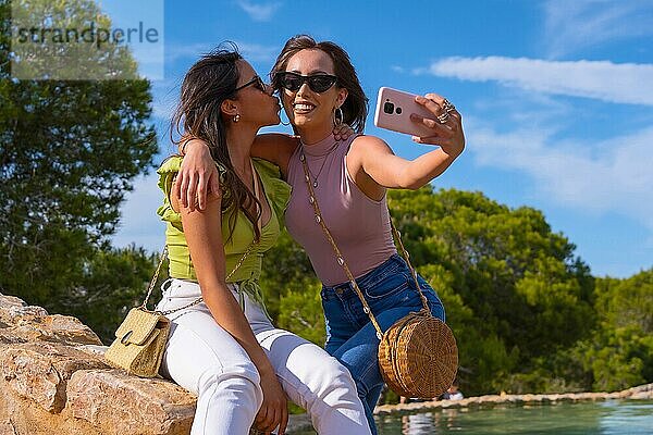 Kaukasische Freundinnen nehmen lächelnd ein Selfie mit dem Telefon im Sommerurlaub in einem Park auf