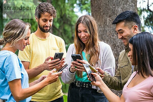 Multiethnische Gruppe mit Telefonen  die im Park das Internet oder soziale Netzwerke beobachten  Technologiekonzept