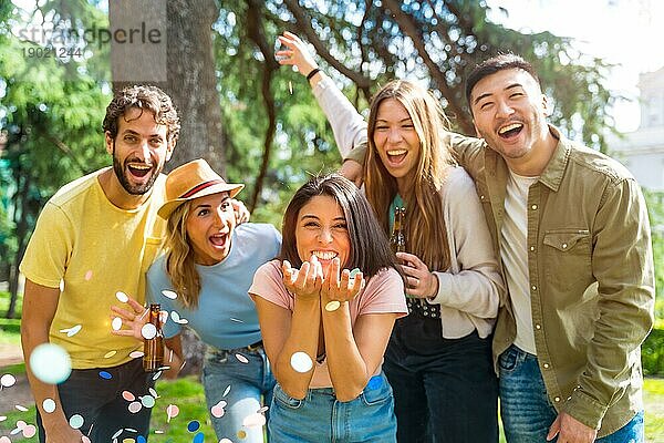 Multiethnische Gruppe von Feiernden werfen Konfetti lächelnd im Park  Spaß mit Freunden Konzept