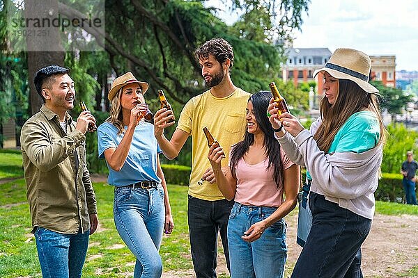 Eine multiethnische Gruppe von Freunden feiert in einem Stadtpark mit Bier. Freunde trinken kaltes Bier