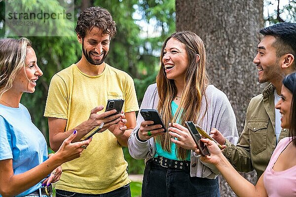 Multiethnische Gruppe lächelnd mit Telefonen im Internet oder in sozialen Netzwerken im Park  Technologiekonzept