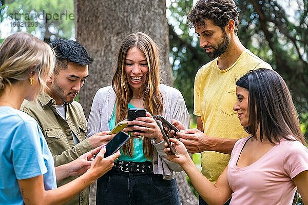 Multiethnische Gruppe mit Telefonen  die im Park das Internet oder soziale Netzwerke beobachten  Technologiekonzept