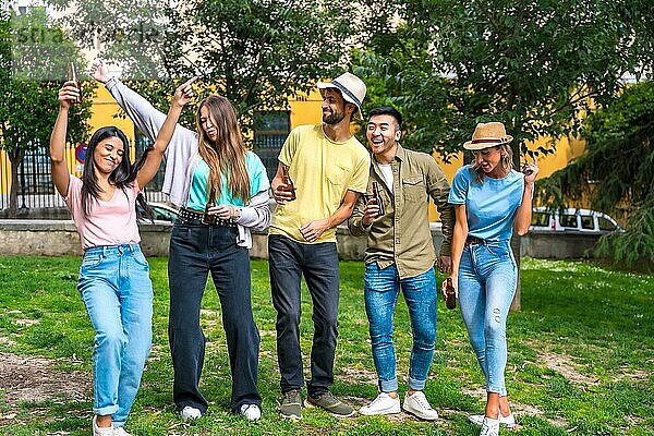 Eine multiethnische Gruppe von Freunden feiert in einem Stadtpark und hat Spaß mit Bierflaschen