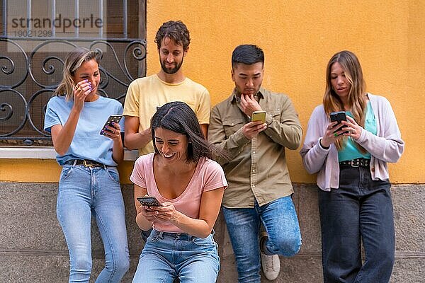 Gruppe von multirassischen Freunden  die lächelnd auf das Telefon in der Stadt schauen