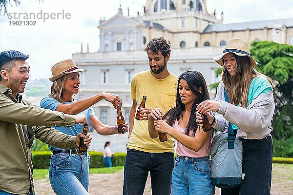 Eine multiethnische Gruppe von Freunden feiert in einem Stadtpark mit Bier