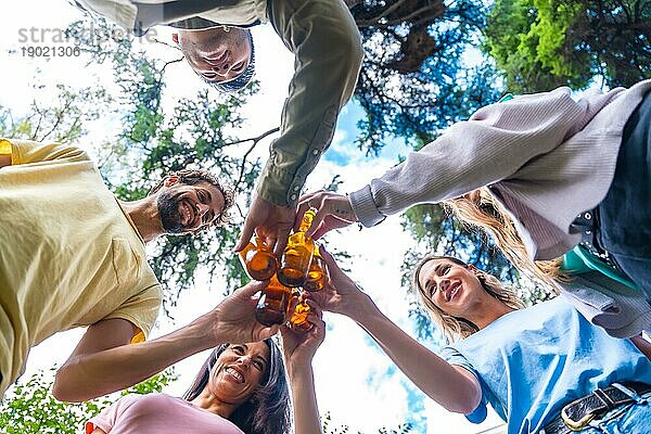 Nadir Aufnahme einer Gruppe multiethnischer Freunde  die im Stadtpark sitzen und mit Bierflaschen anstoßen