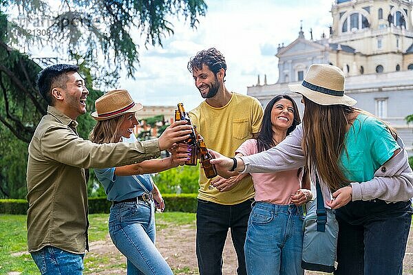 Multiethnische Gruppe von Freunden  die in einem Stadtpark mit Bier feiern und mit den Flaschen anstoßen