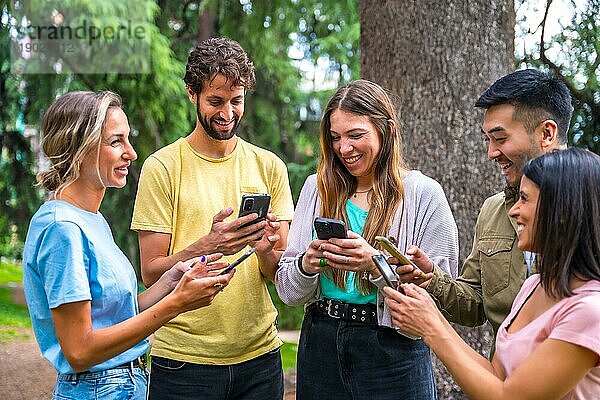 Multiethnische Gruppe lächelnd mit Telefonen im Internet oder in sozialen Netzwerken im Park  Technologiekonzept