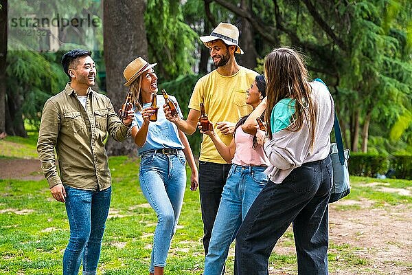 Eine multiethnische Gruppe von Freunden feiert in einem Stadtpark mit Bierflaschen