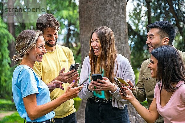 Lächelnde multiethnische Gruppe mit Telefonen  die Internet oder soziale Netzwerke im Park beobachten  Technologiekonzept