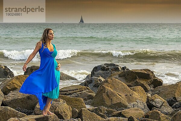 Eine schöne Brünette hispanischen Modell posiert im Freien an einem Strand bei Sonnenuntergang