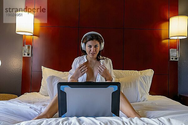 Eine schöne hispanische Frau kommuniziert über den Computer  während sie nackt in einem Schlafzimmer posiert