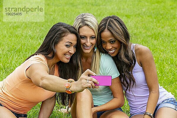 Drei junge Frauen machen ein Gruppenfoto  während sie einen Tag im Park genießen