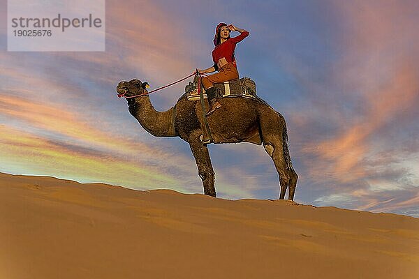 Ein schönes Model reitet auf einem Kamel durch die Wüste Sahara in Marokko