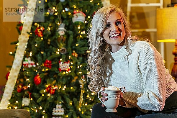 Ein wunderschönes blondes Model genießt die Feiertage zu Hause mit einem Weihnachtsbaum und Geschenken