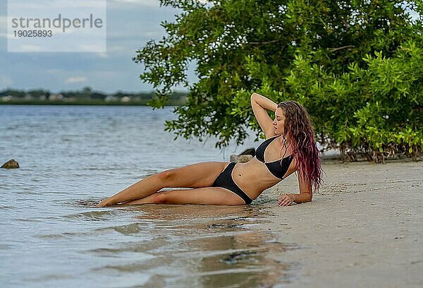 Ein schönes brünettes Bikinimodell genießt das Wetter draußen am Strand