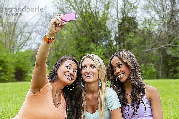 Drei junge Frauen machen ein Gruppenfoto  während sie einen Tag im Park genießen