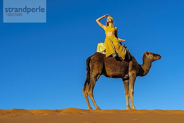 Ein schönes Model reitet auf einem Kamel durch die Wüste Sahara in Marokko