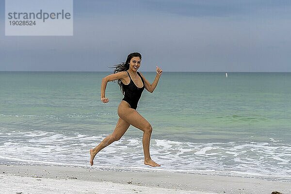 Ein schönes Mixed race Bikinimodell genießt das Wetter draußen am Strand beim Laufen in der Nähe der Brandung