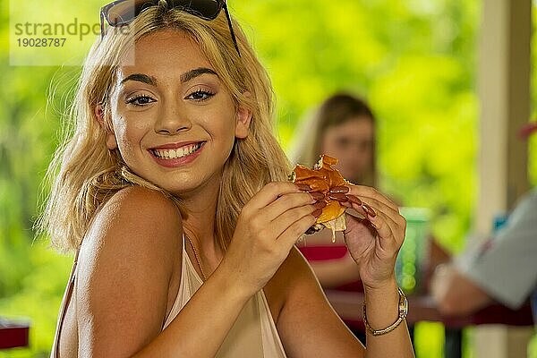 Ein wunderschönes junges blondes Model genießt ihr Mittagessen im Freien  während es während der Covid 19 Pandemie einen Sicherheitsabstand zu anderen Menschen einhält