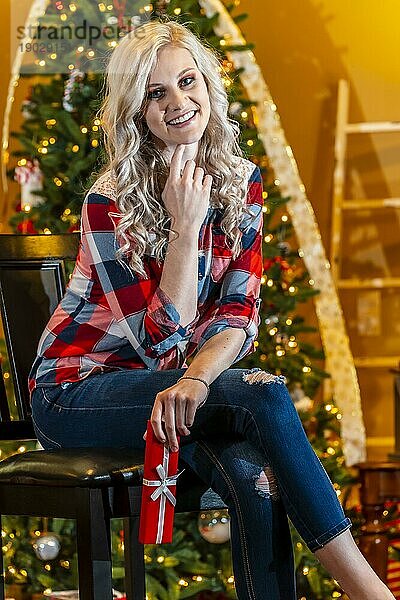 Ein wunderschönes blondes Model genießt die Feiertage zu Hause mit einem Weihnachtsbaum und Geschenken