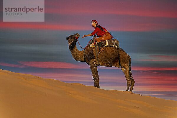 Ein schönes Model reitet auf einem Kamel durch die Wüste Sahara in Marokko