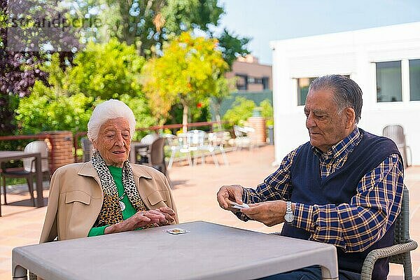 Zwei ältere Menschen  die an einem Sommermorgen im Garten eines Pflegeheims oder Seniorenheims Karten spielen