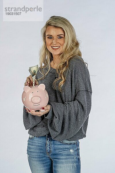 Ein wunderschönes blondes Modell hält ein Sparschwein und spart Geld