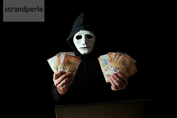 Schwarz gekleideter Hacker mit weißer Maske und schwarzer Kapuze  der Eurobanknoten in den Händen hält  CybercrimeKonzept vor schwarzem Hintergrund