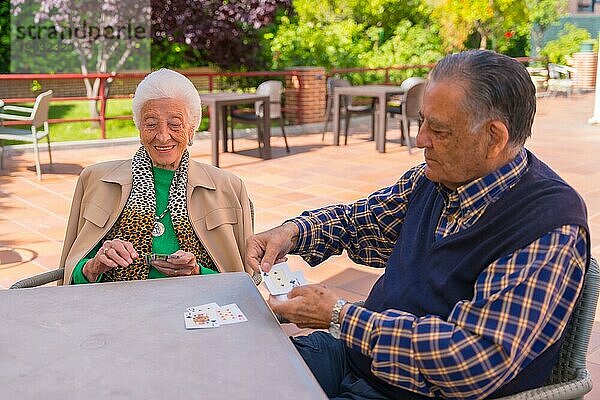 Zwei ältere Menschen  die an einem Sommermorgen im Garten eines Pflegeheims oder Seniorenheims Karten spielen
