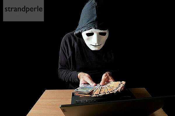 Hacker Mann in schwarz gekleidet mit weißer Maske und schwarzer Kapuze Zählen von Eurobanknoten in seinen Händen  Cybercrime Konzept  vor schwarzem Hintergrund