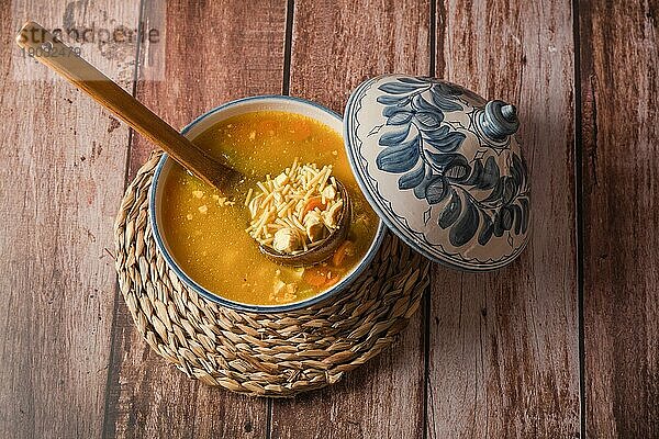 Draufsicht auf eine Suppenterrine mit Hühnernudelsuppe auf einem Holztisch