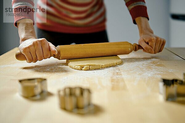 Unbekannte Frau rollt Ingwerteig mit einem Nudelholz auf dem Küchentisch aus (Tiefblick mit selektivem Fokus)