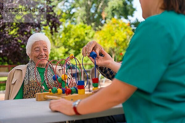 Hände zweier älterer Menschen im Garten eines Pflegeheims oder Seniorenheims  die mit Spielen zur Verbesserung der Beweglichkeit der Hände lächelnd spielen