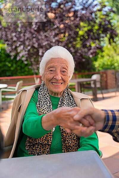 Hände zweier älterer Menschen im Garten eines Pflegeheims oder einer Pension  die sich in einem Moment der Zuneigung an den Händen halten