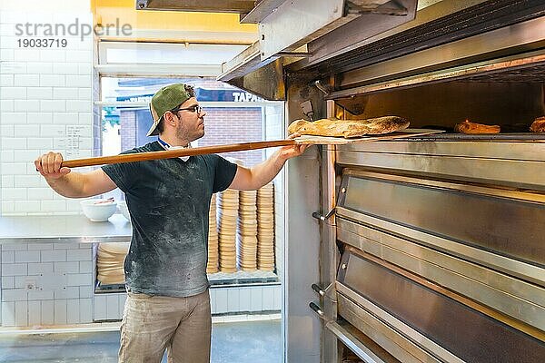 Bäcker in der Werkstatt Handwerksbetrieb beim Backen von Broten im Ofen  Kontrolle des Backvorgangs