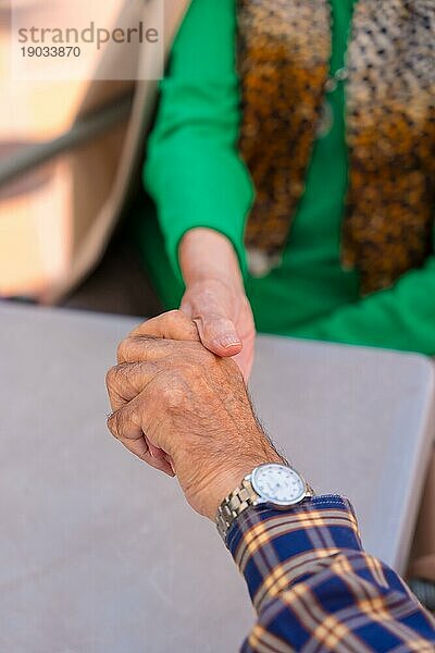 Detail der Hände zweier älterer Menschen im Garten eines Pflegeheims oder Seniorenheims  die sich in einem Moment der Zuneigung an den Händen halten