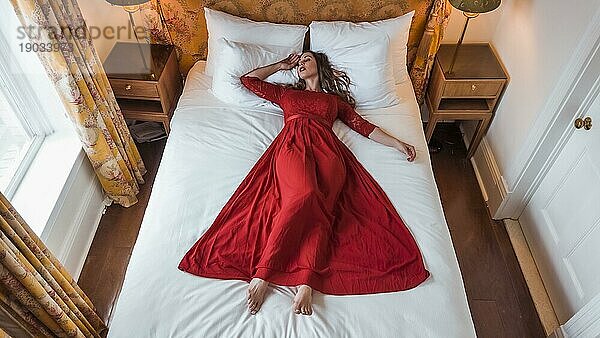 Ein wunderschönes brünettes Modell posiert in einem Kleid in einer Schlafzimmerumgebung