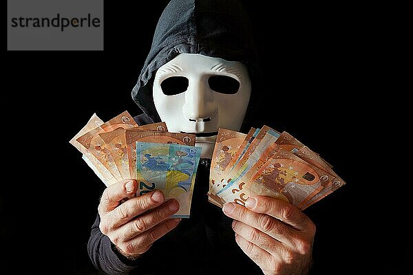 Hacker Mann in schwarz gekleidet mit weißer Maske und schwarzer Kapuze Zählen von Eurobanknoten in seinen Händen  Cybercrime Konzept  vor schwarzem Hintergrund